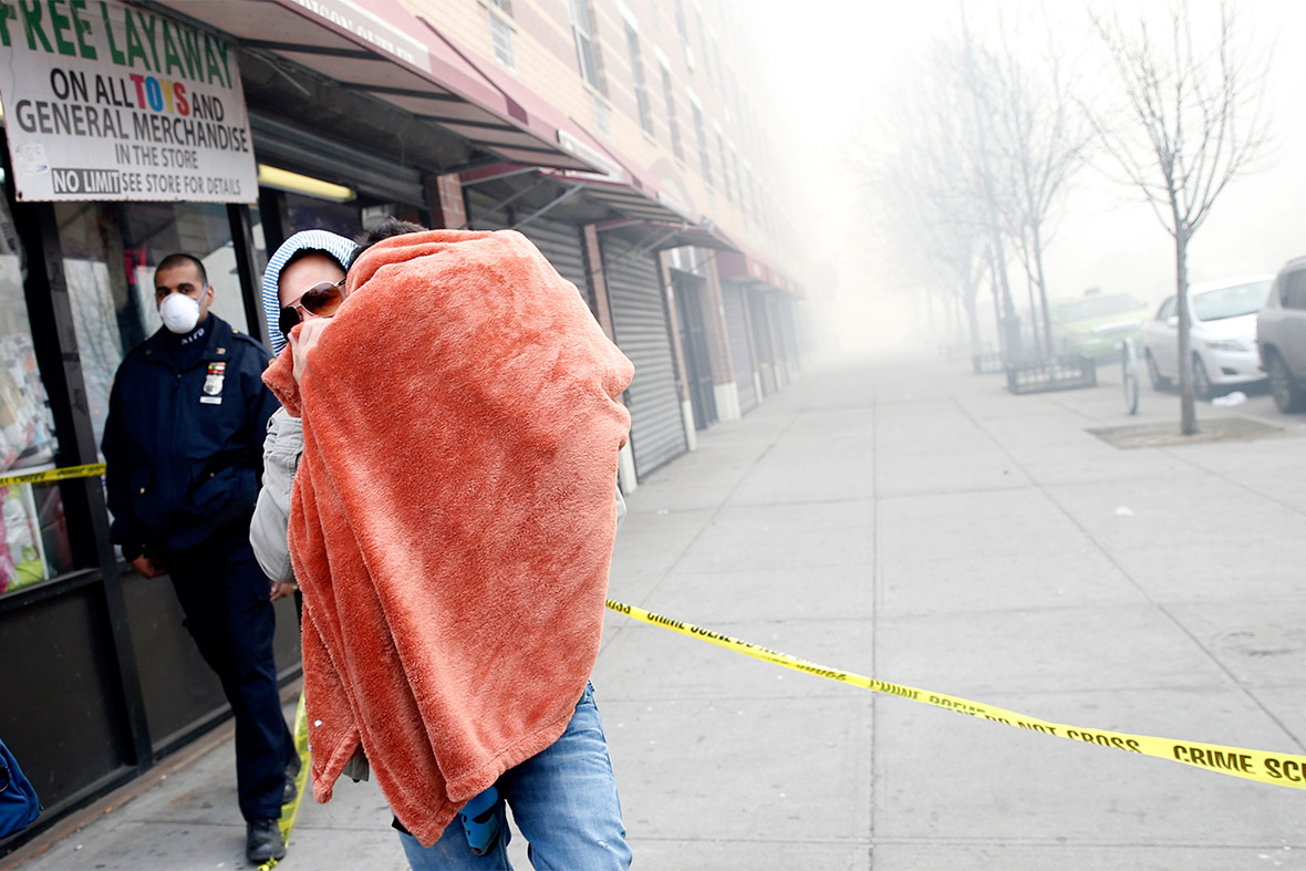 A man carries a child wrapped in a blanket on East 116th street