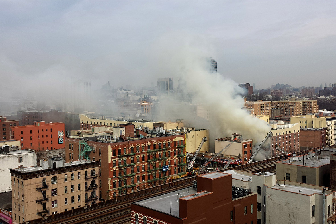 Smoke, dust and steam rise from the scene as firefighters respond to the building collapse at 1646 Park Ave