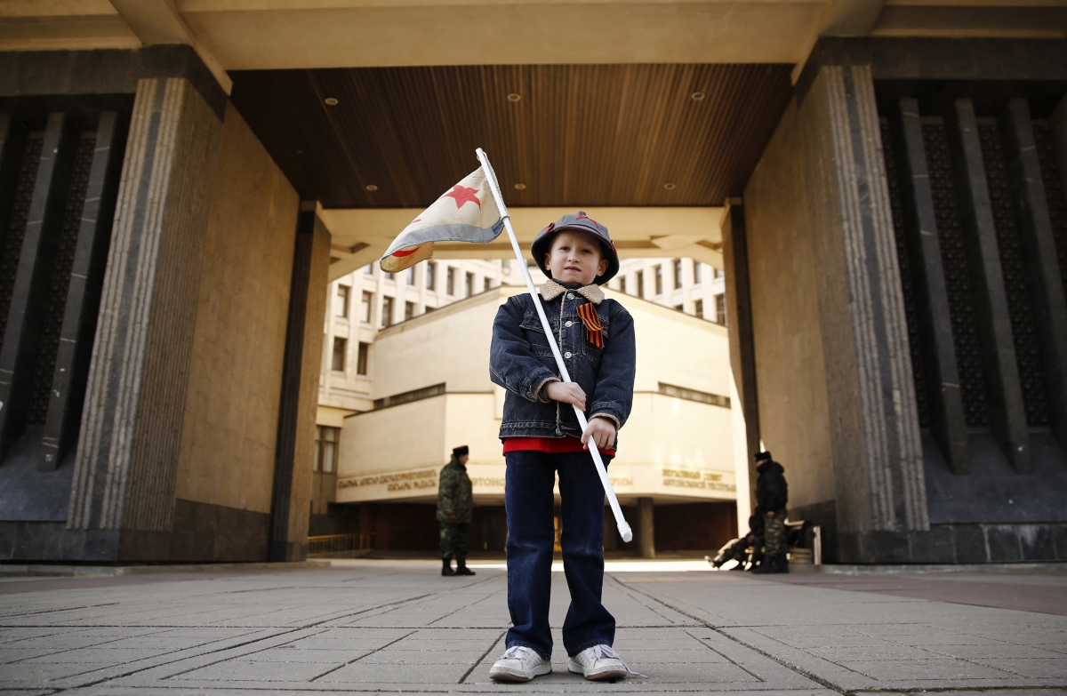 A boy stands in front of the Crimean parliament building, with members of Crimean self-defence units seen in the background, on the eve of a referendum in Simferopol, 15 March 2014 Crimea boy