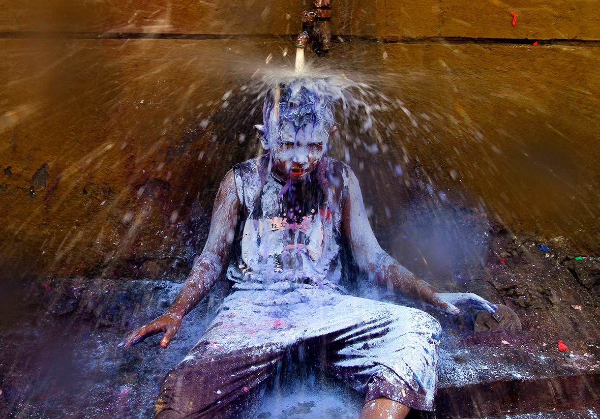 A boy sits under a tap to wash the coloured powder off in Chennai