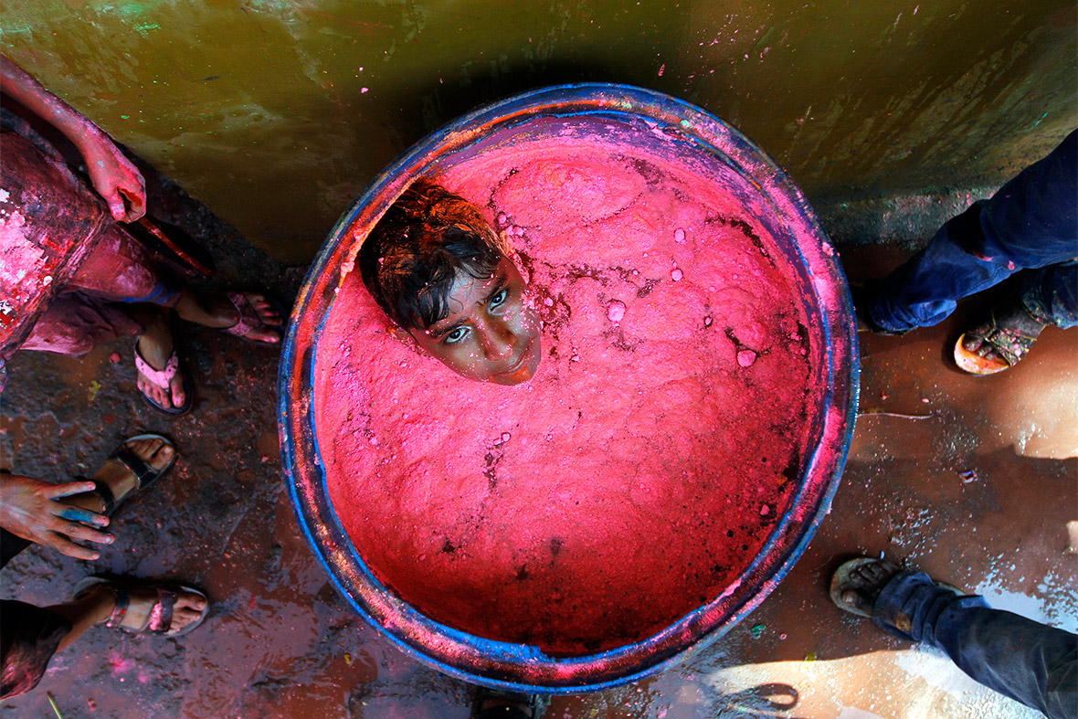 A boy sits in a container filled with coloured powder and water during Holi celebrations in the southern Indian city of Chennai