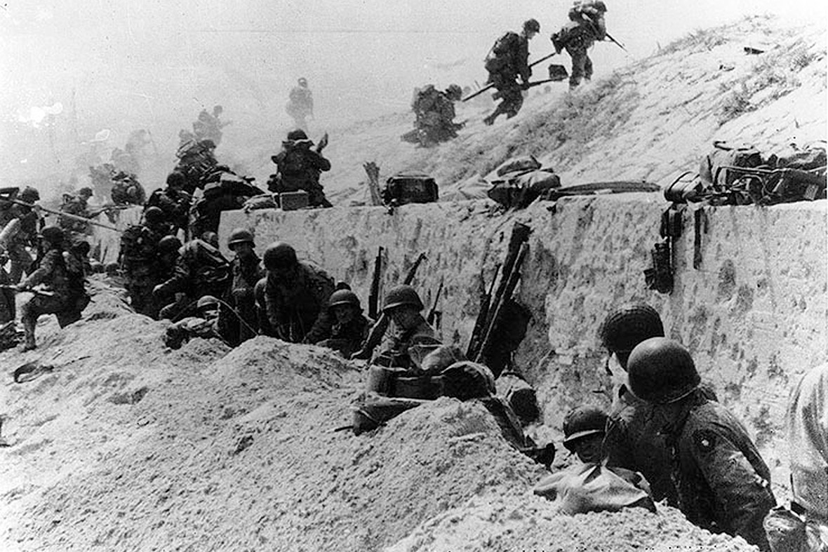 6 de junho de 1944: soldados do Exército dos EUA do 8 º Regimento de Infantaria, 4 ª Divisão de Infantaria, mova ao longo do paredão em Utah Beach depois de chegar em terra na frente de uma parede de concreto perto de La Madeleine, França