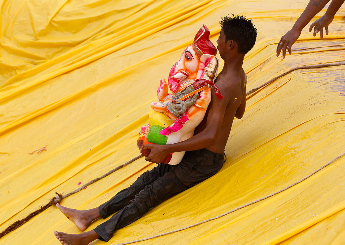 A young man carrying an idol of Ganesh slides down into a pond in the western Indian city of Ahmedabad