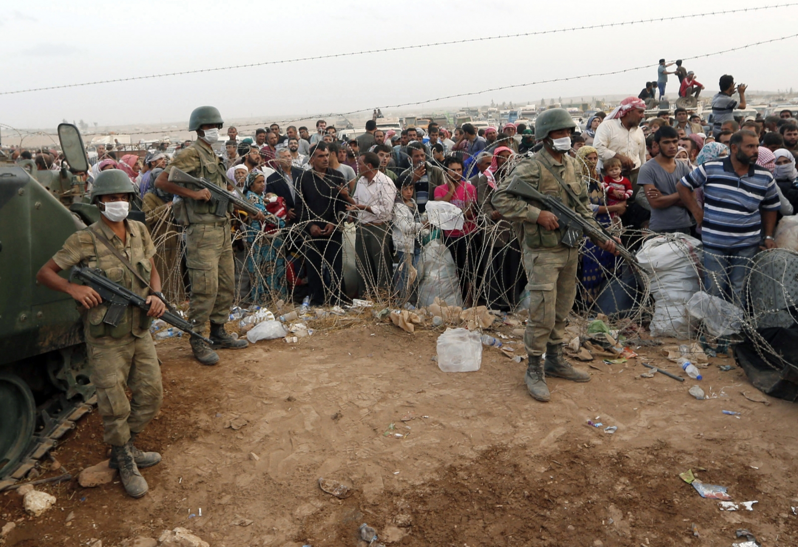 Turkish soldiers stand guard as Syrian Kurdish refugees wait behind the border fences