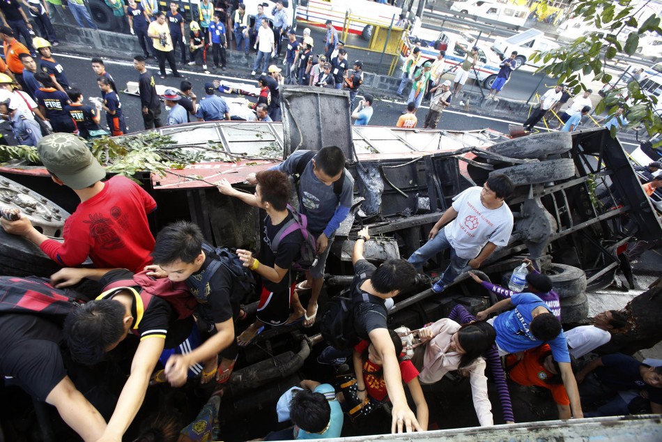 Pedestrians walk on top of an overturned bus as they try to cross the road after the bus fell off an elevated expressway and crashed into a van below in Taguig city, south of Manila