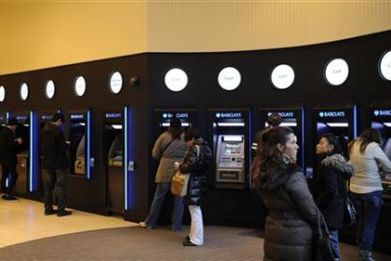 Customers use cash machines in a branch of Barclays bank in London