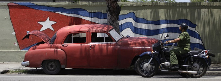 An army officer rides a motorcycle beside a US-made car used as a private collective taxi in Havana.