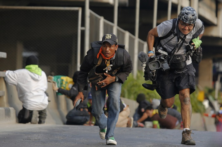 An anti-government protester and a reporter run for cover during a gunfight between government supporters and opponents.
