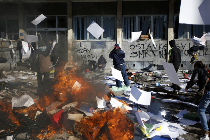 Protesters stand near a fire set in front of a government building in Tuzla