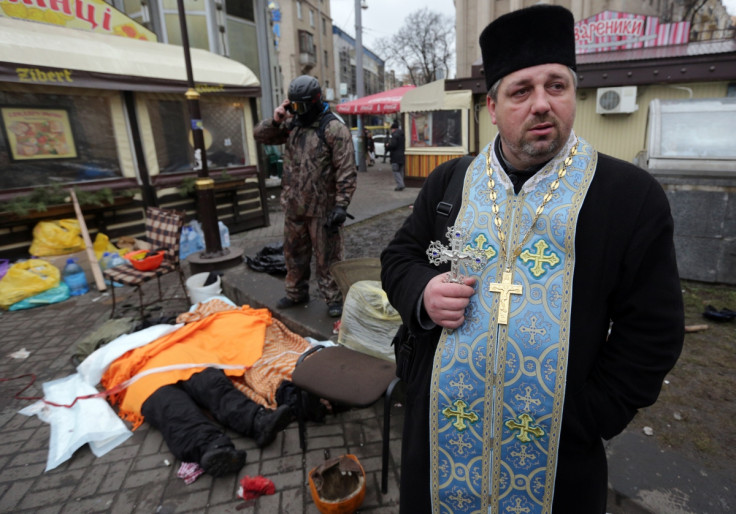 An Orthodox priest holds a cross as dead bodies are seen on the ground following violence in Independence Square in Kiev