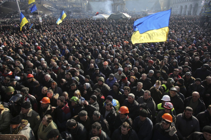 People listen to police officers from Lviv who have joined anti-government protesters as they speak from a stage during a rally in Independence Square