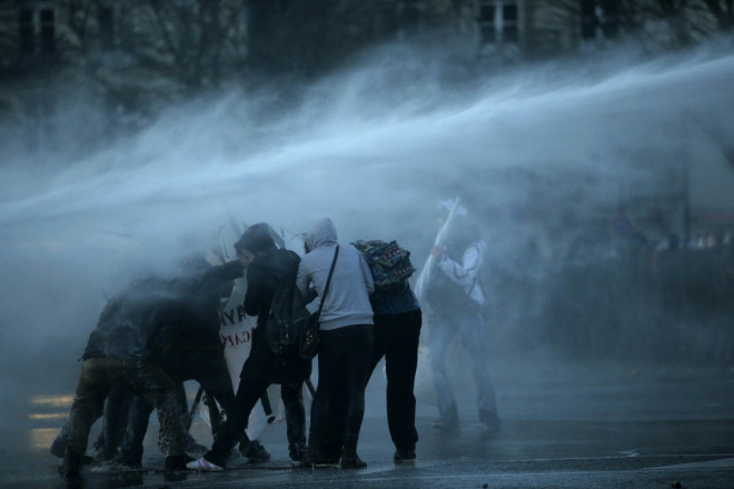 Masked protesters are sprayed by a water canon Masked protesters are sprayed by a water canon