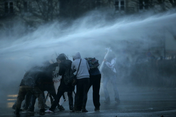Masked protesters are sprayed by a water canon