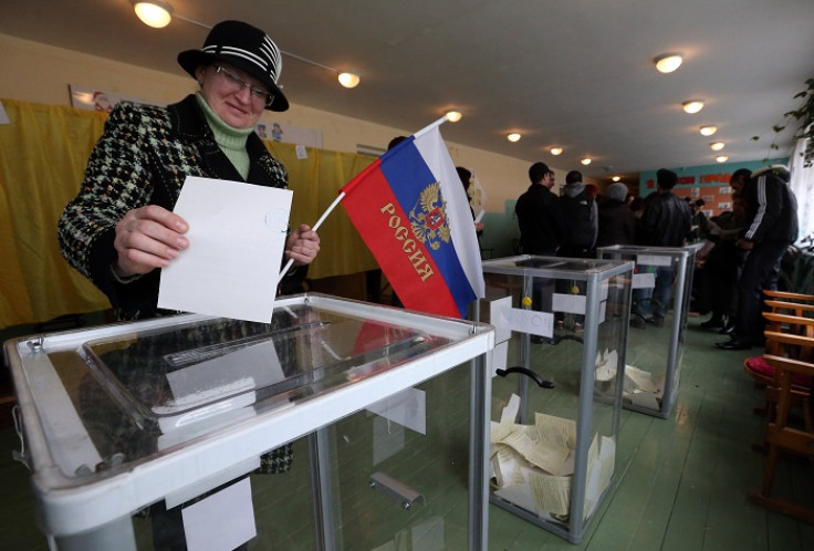 A woman casts her ballot in the Crimea referendum while holding a Russian flag.