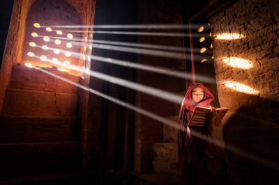 Young monk finds a perfect light source to read his book inside his pagoda in Old Bagan, Burma