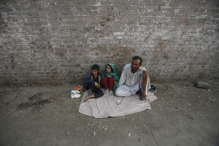 A man sits with his children as he begs along a sidewalk in Peshawar December 11, 2012