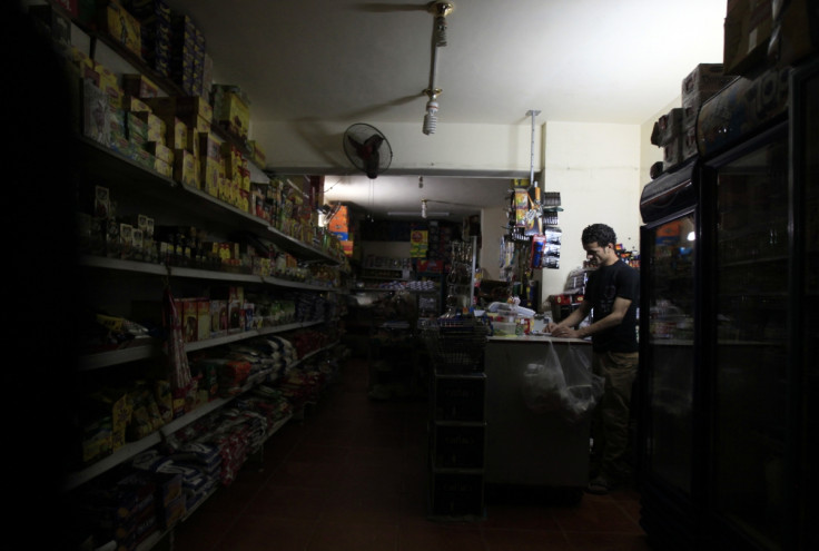 A supermarket seller stands near an emergency light during power outage at his shop in Cairo
