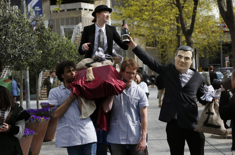 A demonstrator dressed as Britain's Chancellor of the Exchequer George Osborne hands a bottle of champagne to a fellow demonstrator dressed as a banker sitting aloft NHS workers, during a protest outside the Barclays AGM in central London April 24, 2014.