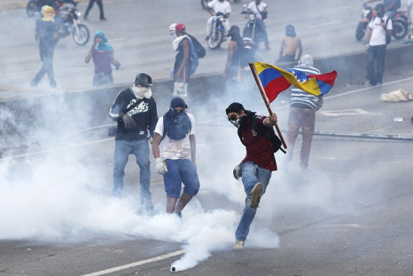 An anti-government protester wields the Venezuelan flag and kicks back a gas canister to police during anti-government demonstrations.