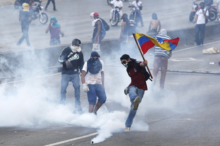 An anti-government protester wields the Venezuelan flag and kicks back a gas canister to police during anti-government demonstrations.