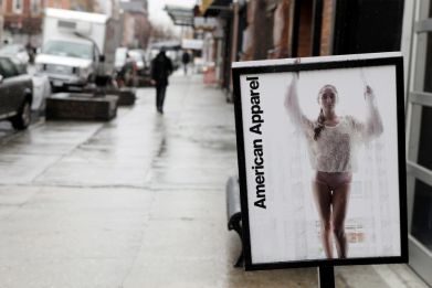 Pedestrians walk past an American Apparel sign outside one of their stores in New York