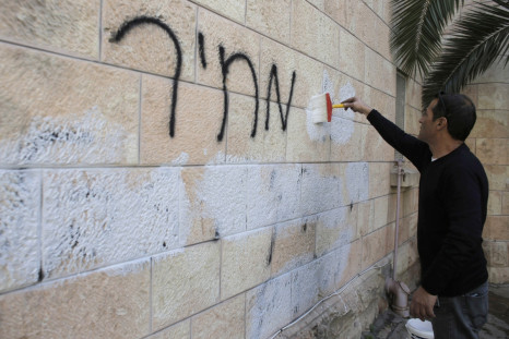 A municipality worker paints over graffiti daubed in Hebrew on a wall of the Romanian Orthodox Church in Jerusalem