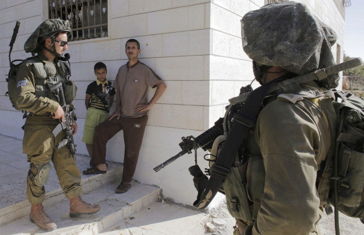Israeli soldiers stand guard next to Palestinians standing outside their house during an operation to locate three Israeli teens near the West Bank City of Hebron