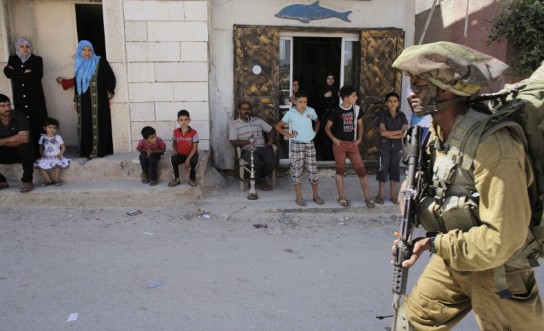 Palestinians watch as an Israeli soldier patrols near the West Bank City of Hebron