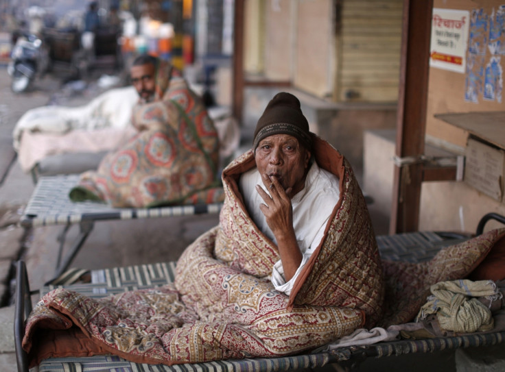 A homeless man smokes as he is wrapped in a quilt at a pavement early morning in the old quarters of Delhi