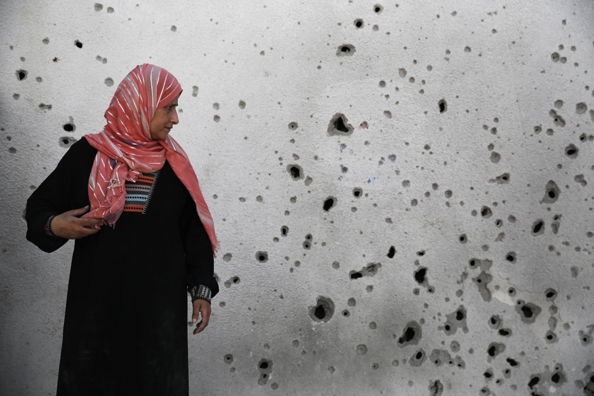 Palestinian woman looks at a shrapnel-scarred wal