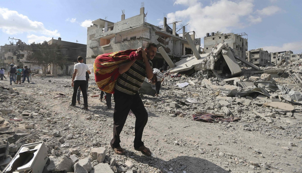 Palestinian man carries his belongings past destroyed houses