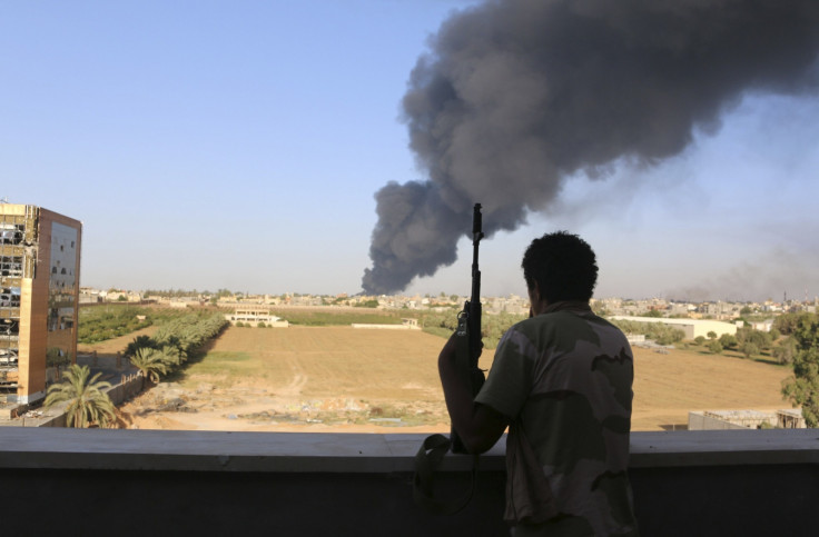 A fighter from Zintan brigade watches as smoke rises after rockets fired by one of Libya's militias struck and ignited a fuel tank in Tripoli