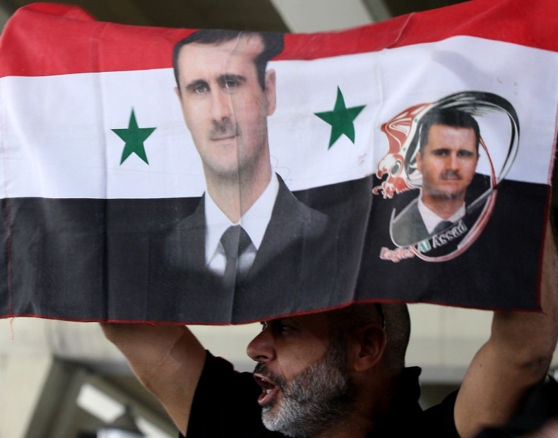 A Syrian man holds his national flag bearing pictures of Syrian President Bashar al-Assad during a pro-regime protest  in Damascus (Getty)