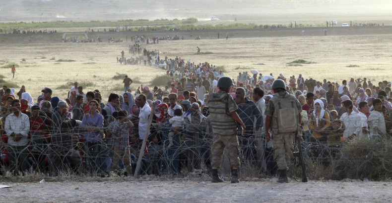 Turkish soldiers stand guard as Syrian refugees wait behind the border fences