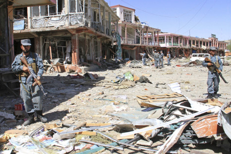 Afghan police stand guard among damaged buildings after a suicide attack in Ghazni Province
