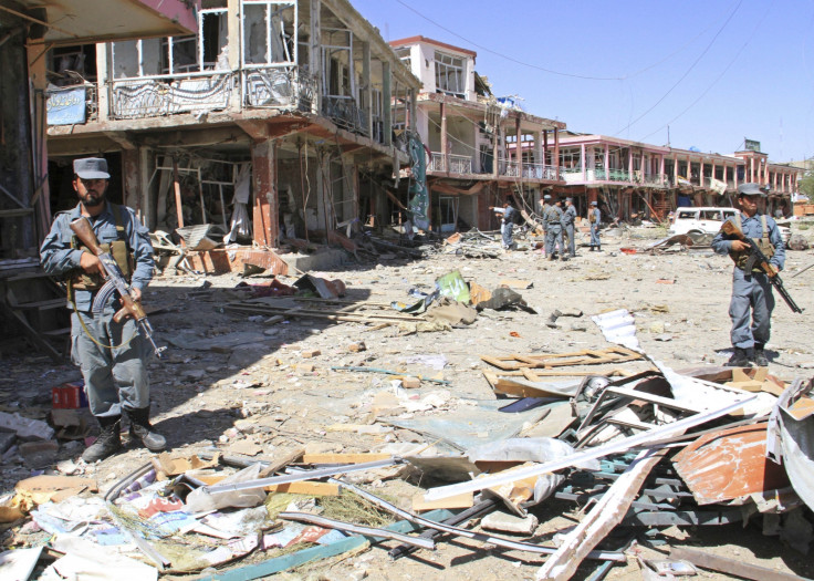 Afghan police stand guard among damaged buildings after a suicide attack in Ghazni Province