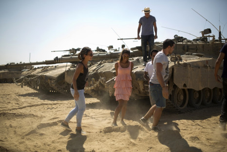 Tourists from Belgium and France walk near tanks at a staging area outside the northern Gaza Strip July 27, 2014.