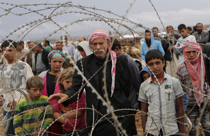 Syrian Kurds wait behind the border fences to cross into Turkey