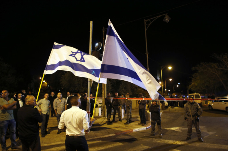 Israelis wave national flags next to security personnel securing an area in Jerusalem where a far-right activist was shot and wounded,