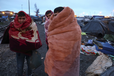 Afghan immigrants use blankets to keep warm near makeshift shelters before French police evacuated them from an improvised camp in Calais, northern France, May 28, 2014.