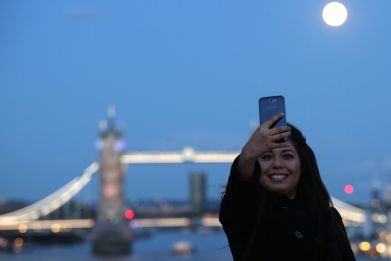 woman takes a selfie as the supermoon rises over Tower Bridge in London