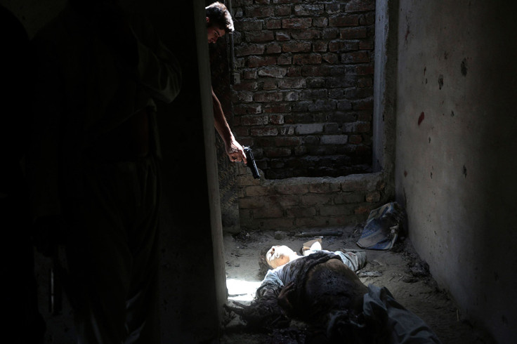 July 17, 2014:  A man points his weapon at the dead body of an unidentified militant, as a way of showing his hatred for insurgents, after an attack on Kabul airport