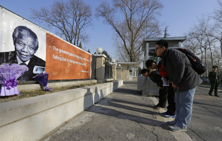 Chinese residents bow to a banner bearing a picture of former South African President Nelson Mandela as they pay tribute in front of the South African Embassy in Beijing