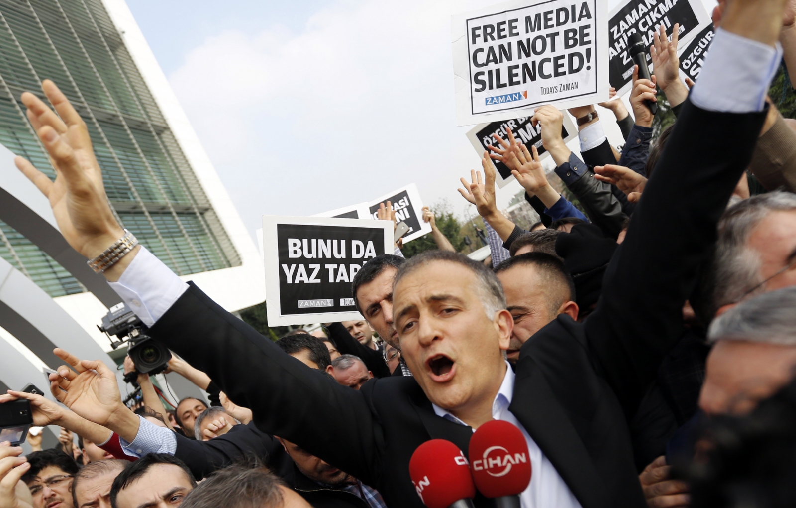 Zaman editor-in-chief Ekrem Dumanli, surrounded by his colleagues and plainclothes police officers (C), reacts as he leaves the headquarters of Zaman daily newspaper in Istanbul