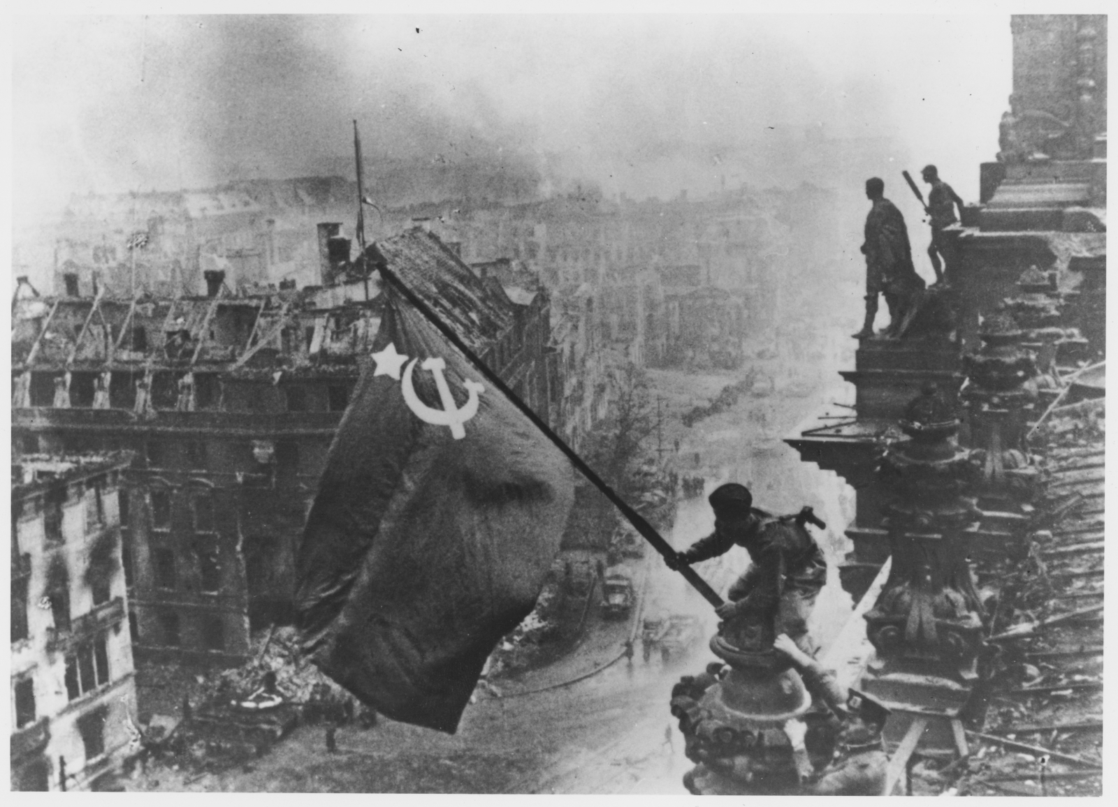 Russian soldiers flying the Red Flag, made from table cloths, over the ruins of the Reichstag in Berlin
