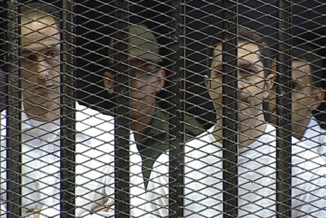 Alaa and Gamal Mubarak stand in the courtroom during their trial at the Police Academy in Cairo