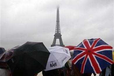 Tourists protect themselves from the rain under umbrellas in front of the Eiffel tower in Paris as they visit the French capital during summer holidays