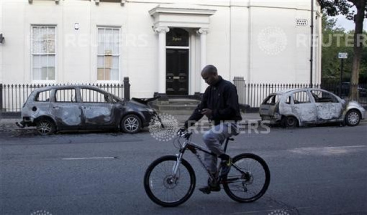 A man looks at his mobile phone as he cycles past two burned out cars in the Toxteth area of Liverpool