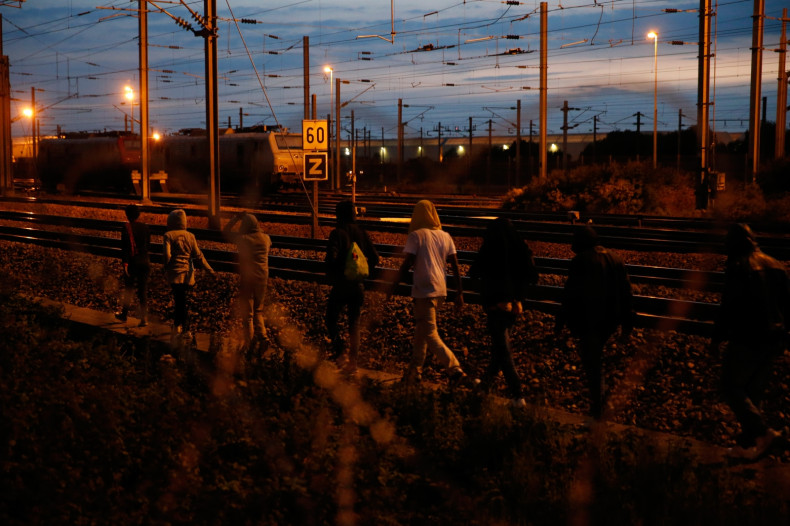 Migrants walk along the tracks