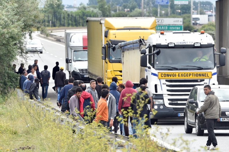 Migrants stand as lorries drive past